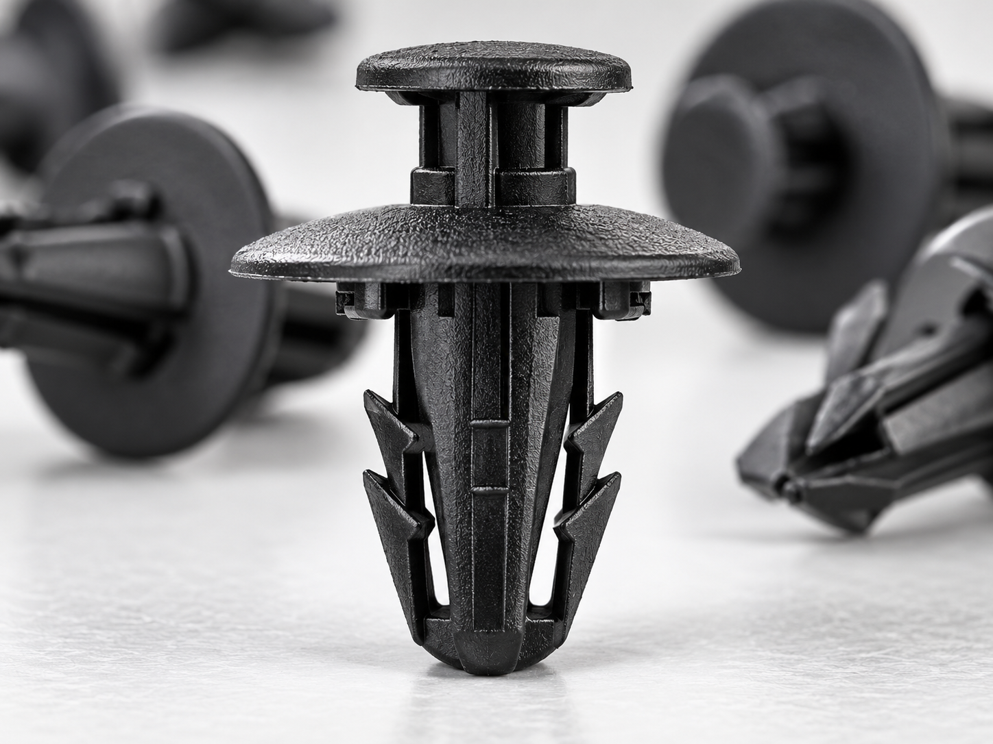 Close-up of an automotive plastic fastener showing flexible locking arms, retaining barbs, and snap-fit features.